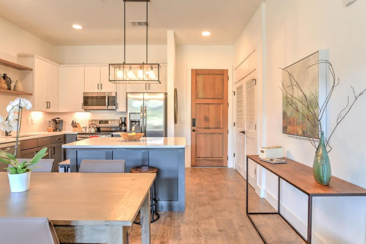 A spacious kitchen-dining area featuring a central kitchen island and a nearby dining table, with tasteful artwork and a warm, welcoming atmosphere. The layout encourages seamless flow between cooking and dining activities.