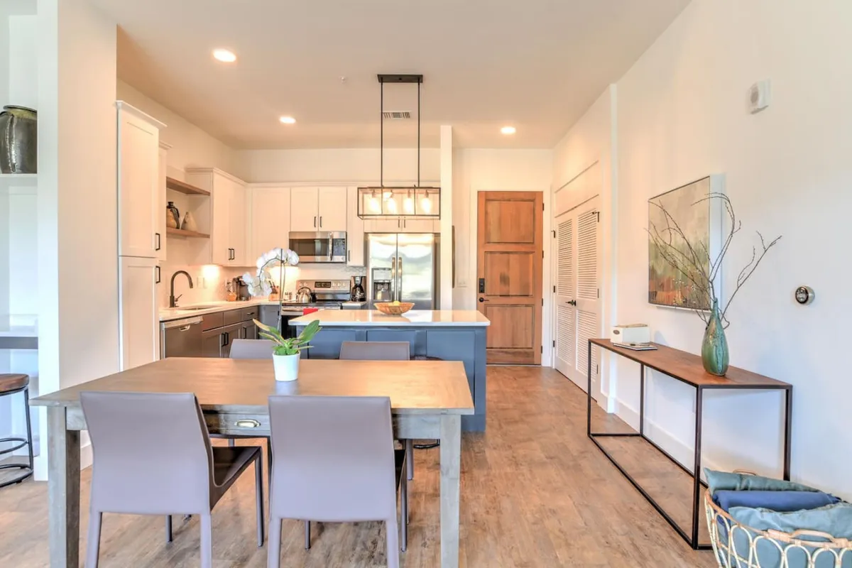 This image showcases a warmly lit dining table and modern kitchen island, set against the backdrop of stylish artwork on the wall. The inviting and cozy atmosphere suggests a functional yet comfortable space for dining or informal meetings.