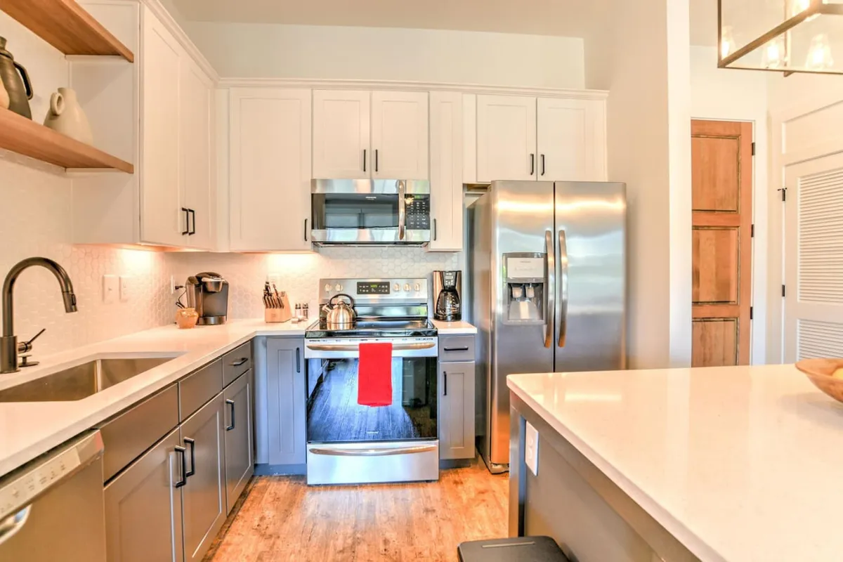 A modern kitchen with gleaming stainless steel appliances, red kitchen towel adding a touch of warmth, and open shelving decorated with stylish accents. The space is inviting and contemporary, ideal for cooking and entertaining.