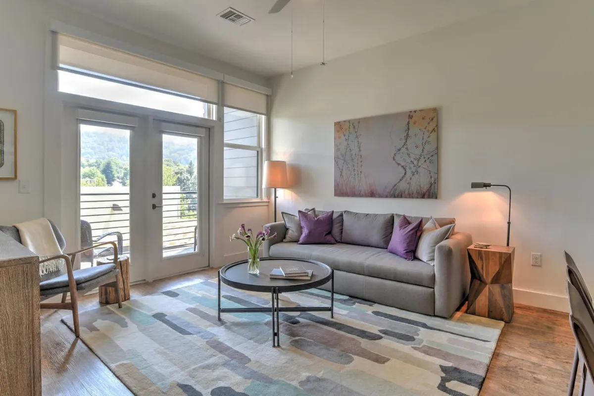 A cozy living area featuring a plush sofa, a stylish coffee table, elegant artwork, and a vase of fresh flowers. The layout feels open and inviting, with natural light enhancing an ambiance perfect for relaxing or enjoying quiet moments together after a day exploring the city.